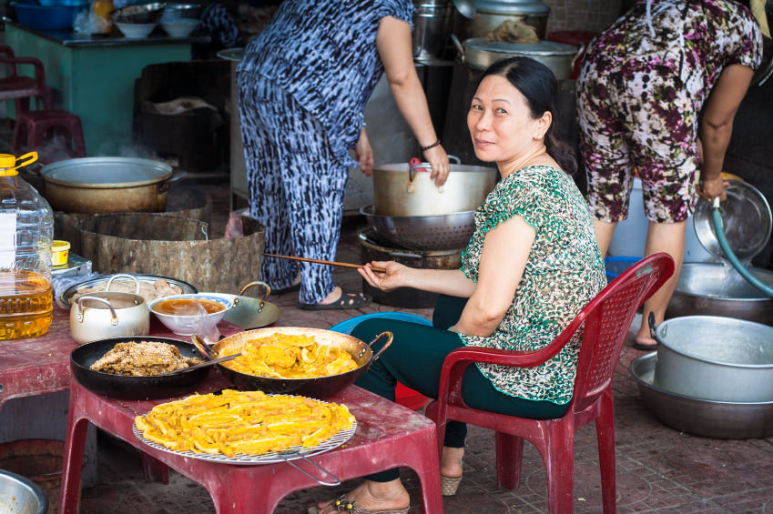 Title photo of the cost breakdown of living in Vietnam: a middle-aged Vietnamese woman sitting next to exotic dishes of food, which she has for sale.