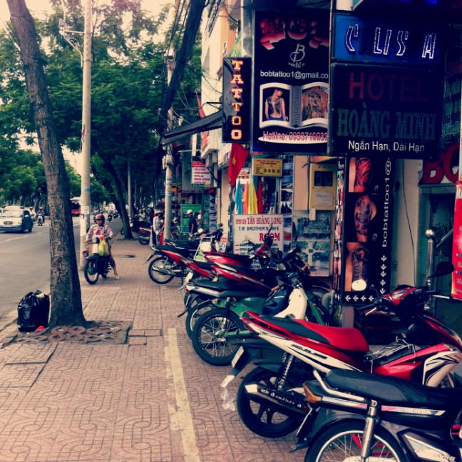 A street of Ho Chi Minh City, rows of motorbikes are parked outside modern-looking shops.